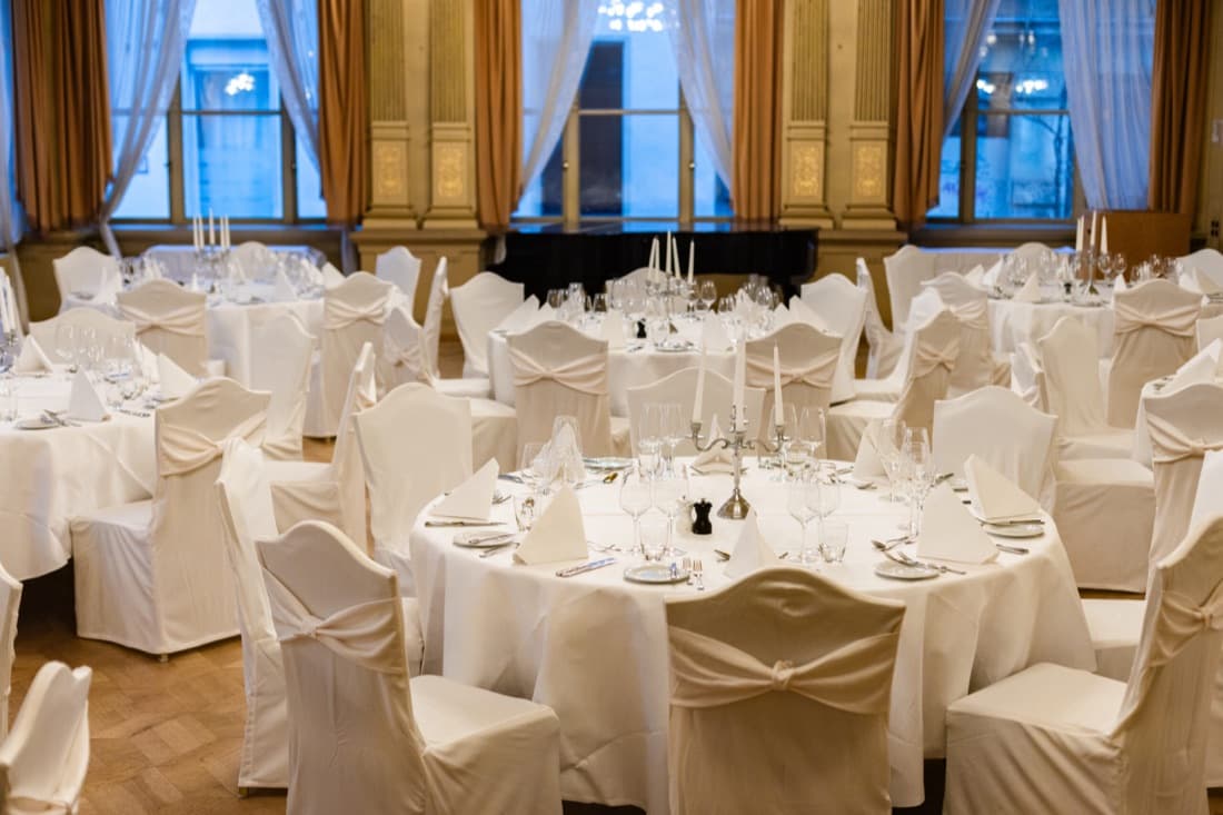 Hochzeitstafeln mit weißen Hussen im Spiegelsaal am Abend